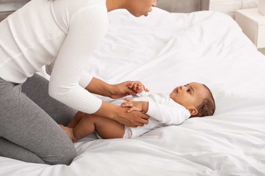 African Mom Doing Gymnastics To Baby In Bedroom, Cropped