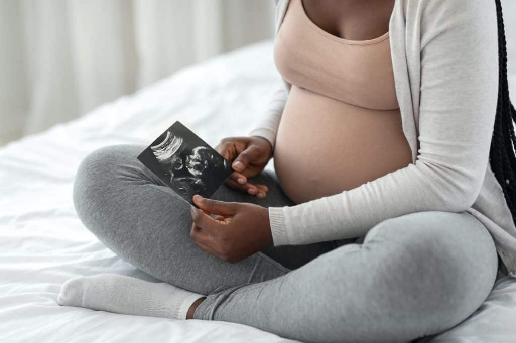 Fetal Development. Pregnant african woman looking at baby ultrasound scan at home
