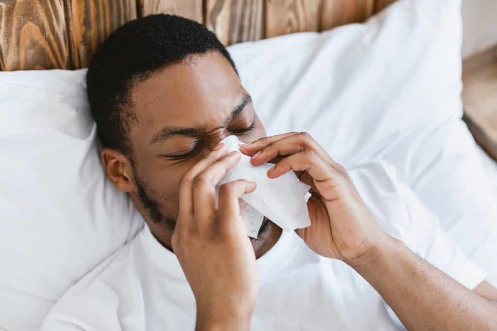 Sick African Guy Blowing Nose In Tissue Lying In Bed