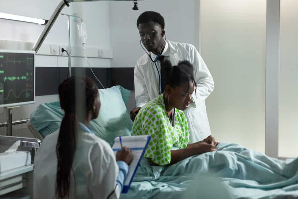 Team of african ethnicity doctors examining patient in hospital ward