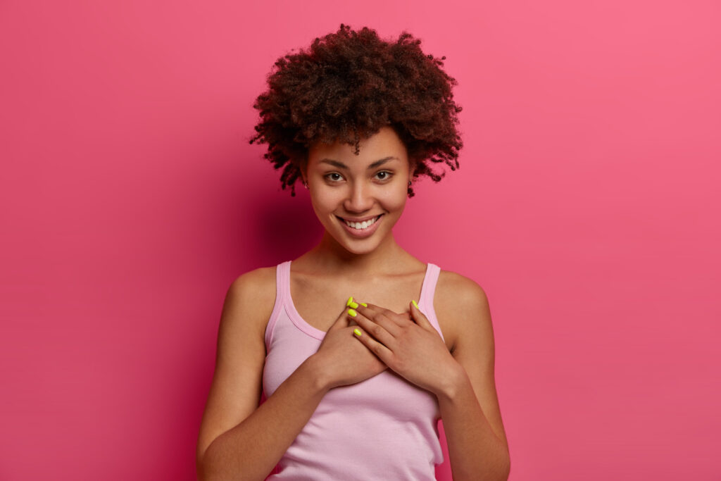 touched pleased lovely woman hears heartwarming story presses hands heart feels thankful promises you smiles gently wears casual clothes appreciates nice gift poses rosy wall