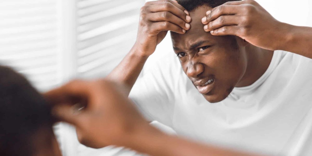 Worried Black Man Examining Face Looking At Wrinkles In Bathroom